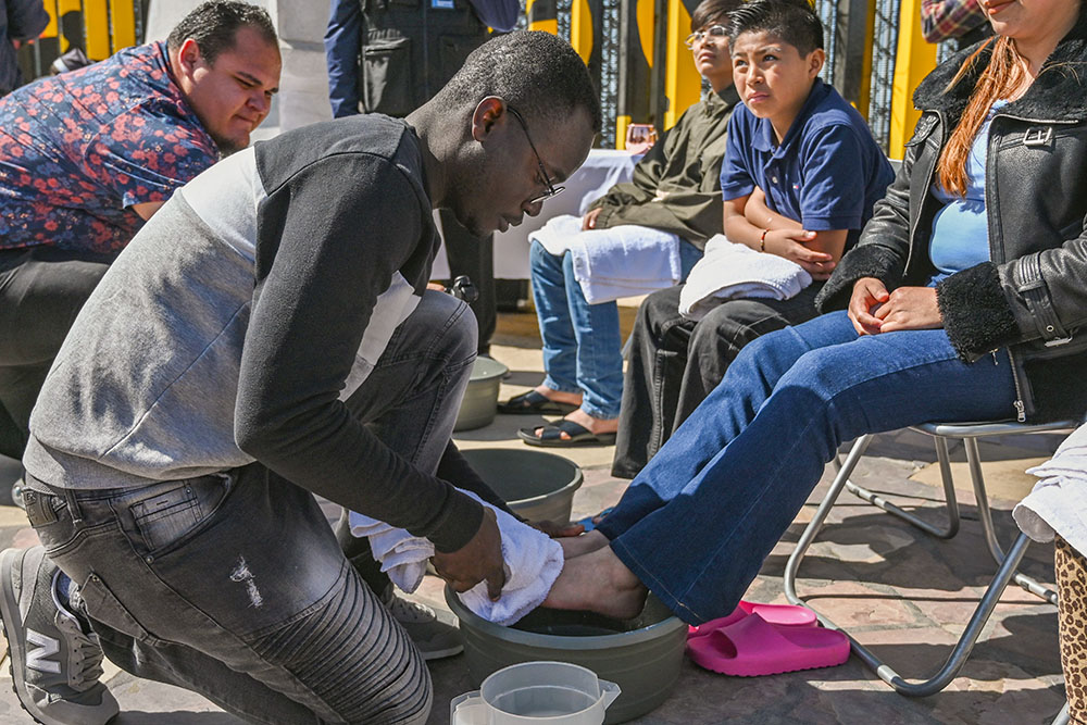 Haitian migrant and volunteer Djephy Wood Denios from La Casa del Migrante in Tijuana, Mexico, cleans the feet of a woman during the annual washing of the feet ceremony on Holy Thursday at Tijuana's Friendship Park circle on the U.S.-Mexico border April 17, 2025. (OSV News/Carlos A. Moreno)