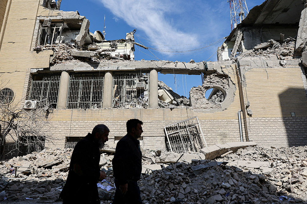 People walk past damaged buildings in Tehran, Iran, March 4, 2026, following a strike on a police station, amid the U.S. and Israel-Iran war. (OSV News/WANA via Reuters/Majid Asgaripour)