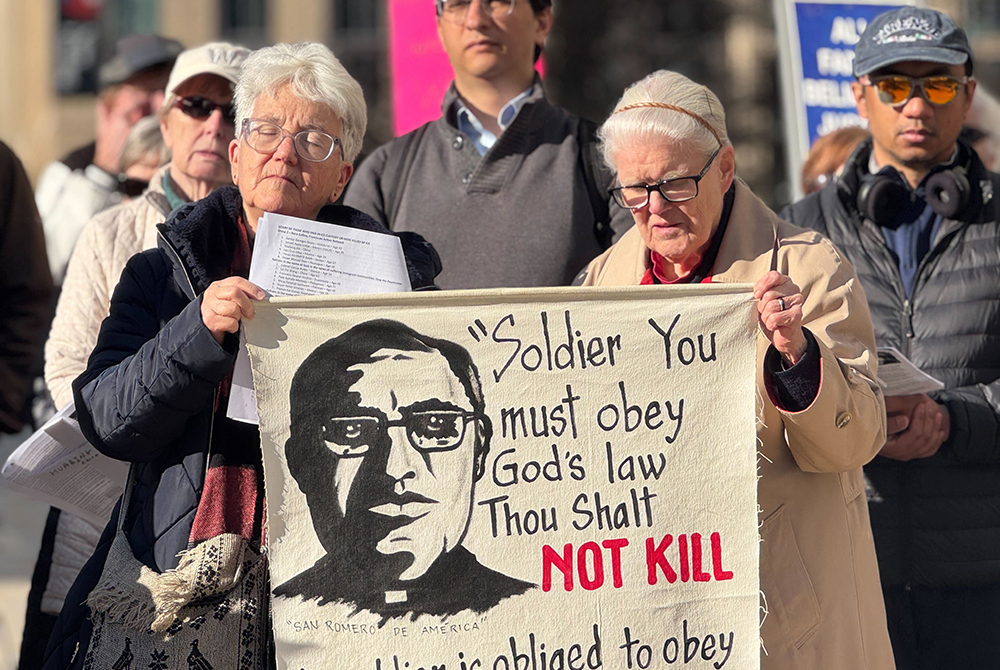 Religious of the Sacred Heart Sr. Diane Roche, left, helps hold a banner with the image and words of St. Oscar Romero, as she prays March 24, 2026 in front of the headquarters of U.S. Immigration and Customs Enforcement. She celebrated Romero's feast day by demanding that the agency put a stop to the violent tactics of some of its agents. (GSR photo/Rhina Guidos)