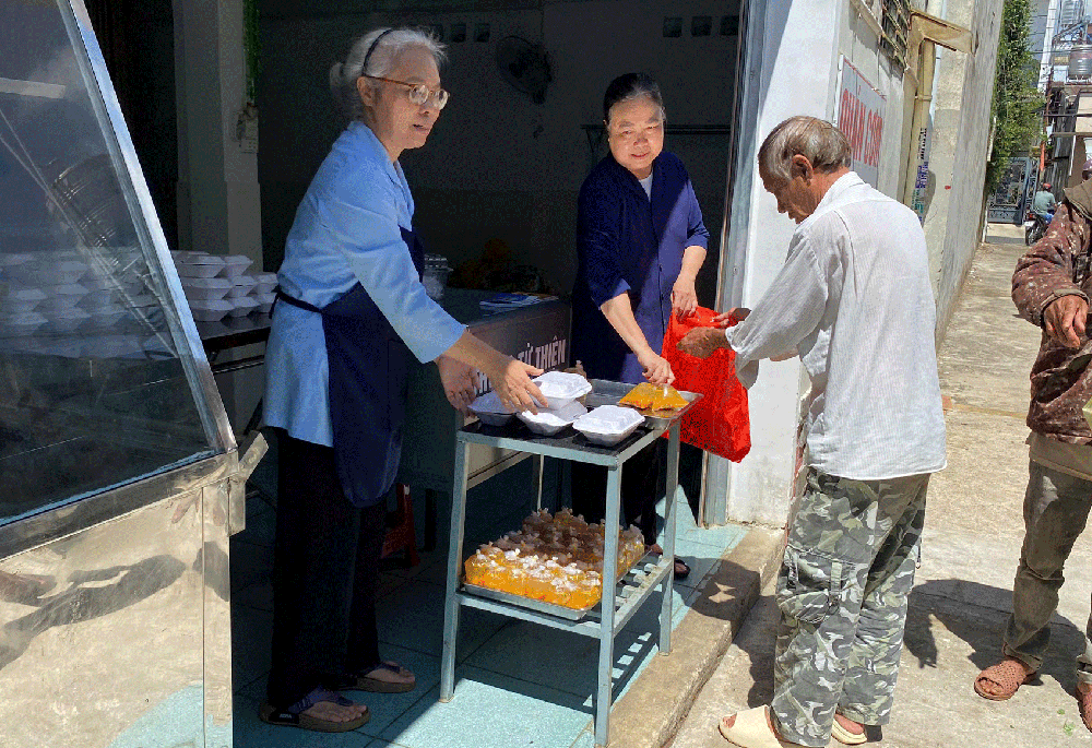 Sr. Trần Thu Hà and Sr. Nguyễn Thị Hường, of the Lovers of the Holy Cross of Dalat greet people as they line up for hot meals at the Kitchen of Love in Bao Loc, Lam Dong, Vietnam, on May 5, 2023. (Sr. Nguyễn Hồng Ân)
