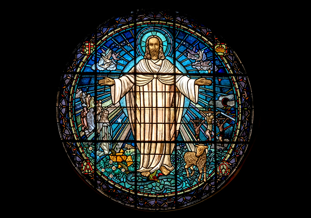 Jesus is rendered in a stained-glass window that shines bright in a dark room. (Unsplash/Paul Zoetemeijer)