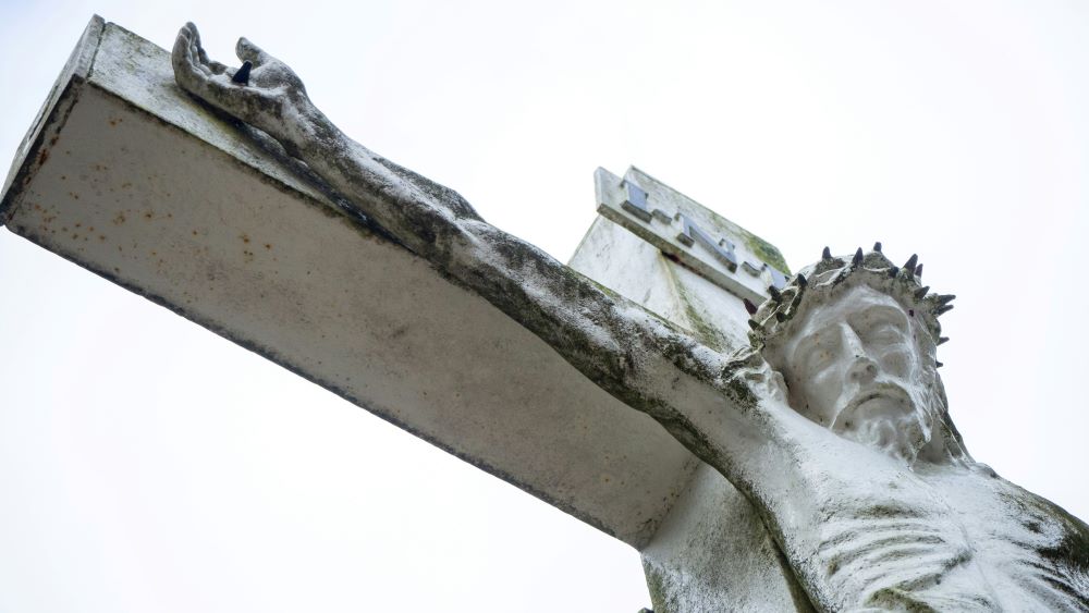 portion of a cement sculpture of crucifox shows Jesus' head and arm. 