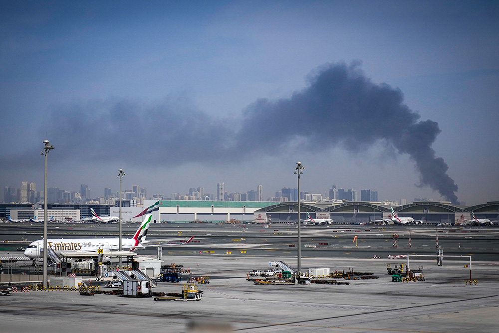 A plume of smoke caused by an Iranian strike is seen in the background as Emirates planes are parked at Dubai International Airport after its closure in Dubai, United Arab Emirates, March 1, 2026. (AP/Altaf Qadri)