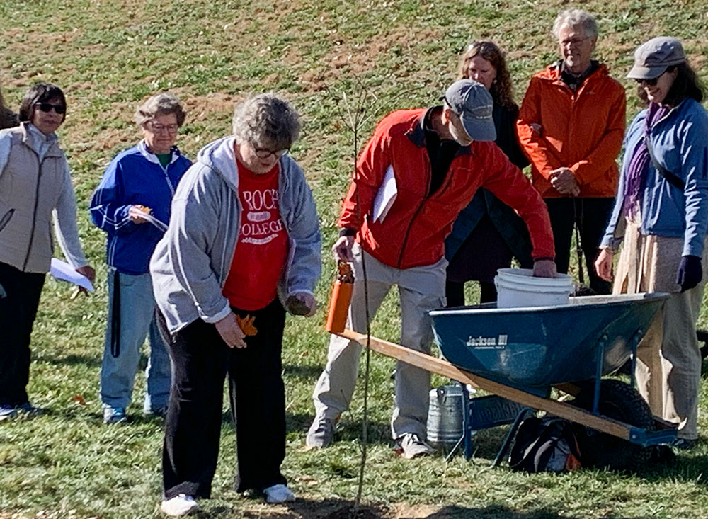 Sister of Divine Providence Judy Connor, at center in red, adds soil to the hole where a white oak tree is being planted on the sisters' property near Pittsburgh. On the left are Srs. Betsa Palomino and Donna Marie Gribschaw. To the right are EcoVillage members Sam Spofforth, Mel Scott, Stu Bush and Rachelle Nordman. (Courtesy of Stefani Danes)