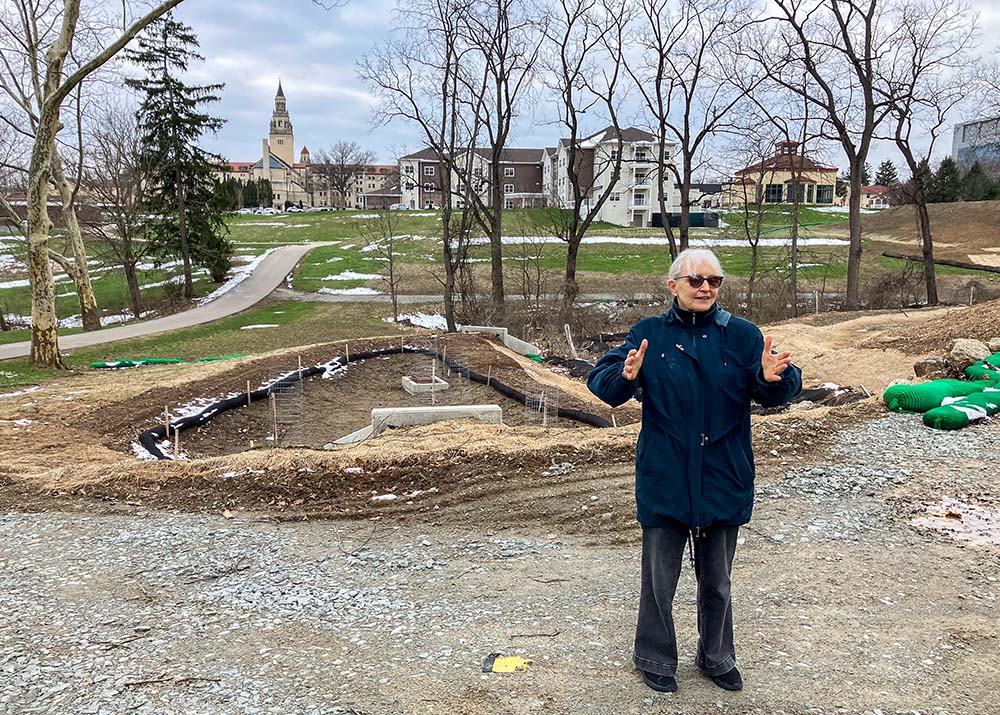 Stefani Danes stands on the Rachel Carson EcoVillage's construction site. The building with a high tower in the background is the Sisters of Divine Providence's 100-year-old convent, now part of La Roche University. (Jennifer Szweda Jordan)