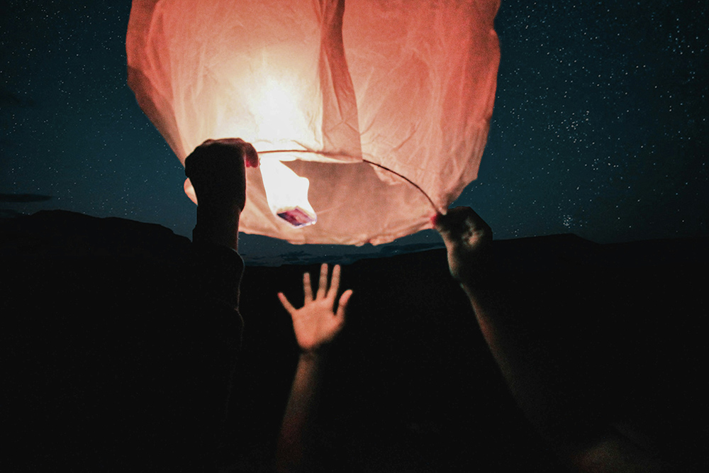 Hands letting go of a floating lantern (Unsplash/David Ananda)
