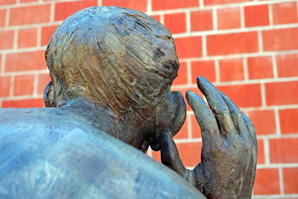 Sculpture of back of a person's head, hand cupping ear.