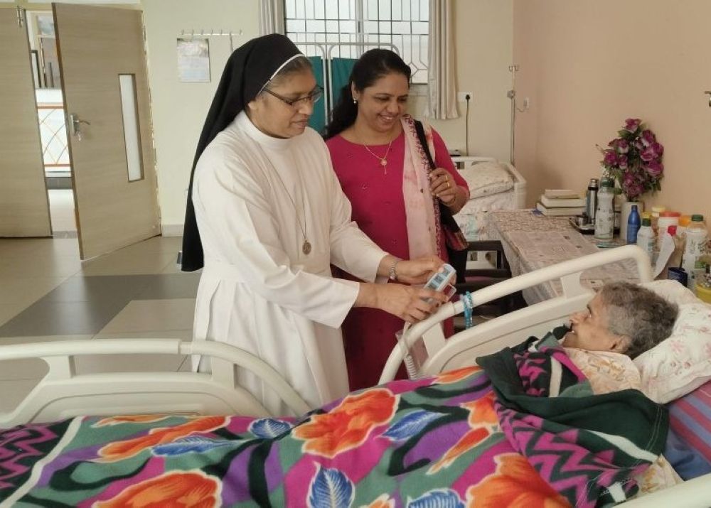 Sr. Roseline Koonthanishiriyil, coordinator of the retired sisters' community at Elizabeth Care Home in Bengaluru, southern India, cares for a bedridden sister as a visitor looks on. (George Kommattam)