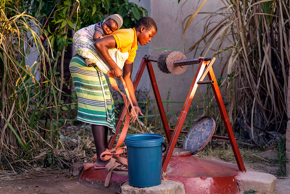 A woman with a baby strapped on her back fetches water from a well in Epworth, a poor neighborhood on the outskirts of Harare, Zimbabwe, June 15, 2022.(AP/Tsvangirayi Mukwazhi)