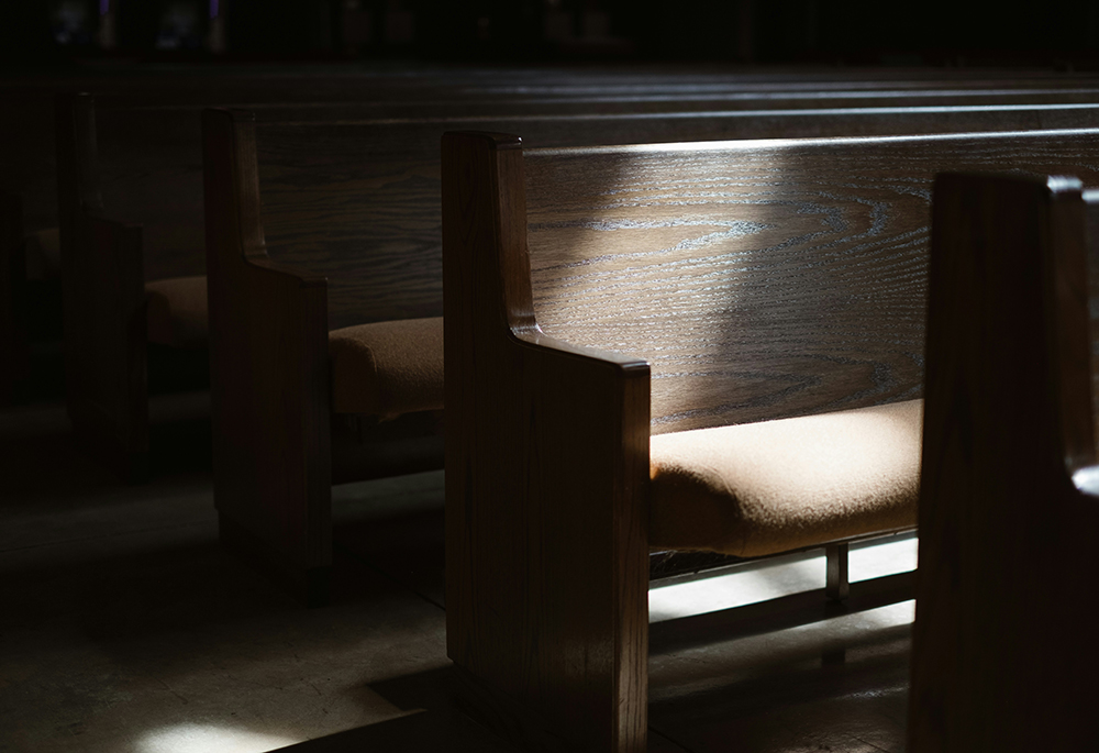 Light shines upon a church pew in a dimly lit church interior. (Unsplash/Josh Applegate)