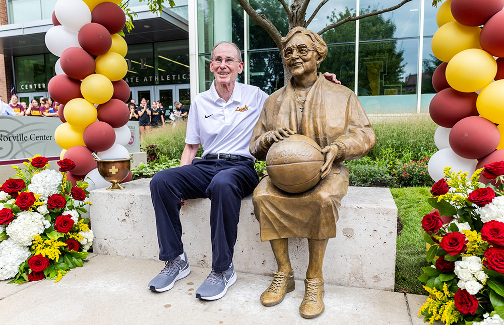 Tom Hitcho, Loyola senior associate athletics director and longtime friend of Sr. Jean Schmidt, was the first to sit next to the statue after it was unveiled Aug. 21, 2026, at Loyola University Chicago. (Courtesy of Loyola University Chicago)