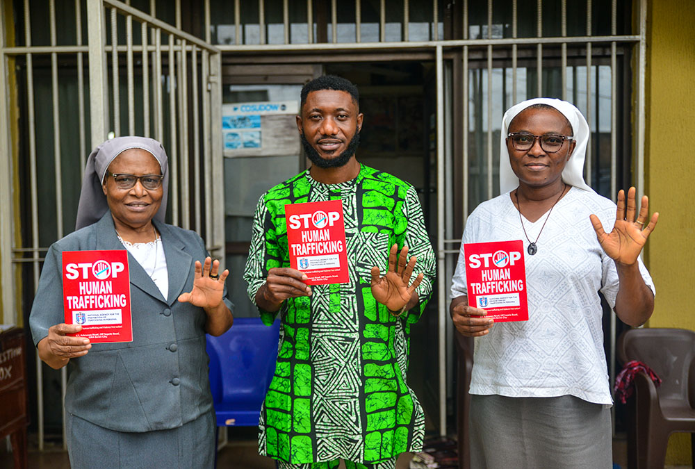 From left, Sr. Justina Odunukwe, staff member Wisdom Ugochukwu Umunakwe and Sr. Helen Omeya display an anti-trafficking poster outside the office of the Committee for the Support of the Dignity of Women in Benin City, Nigeria. (Patrick Egwu)