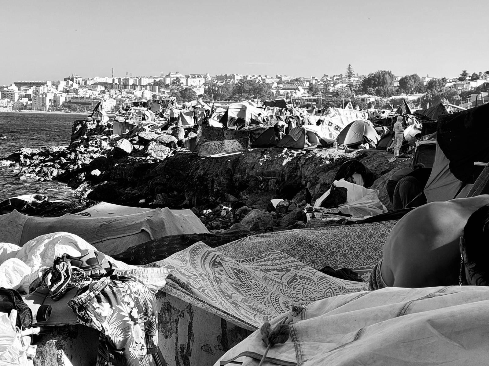 Chozas improvisadas con cartón y plástico ocupan el primer plano de la imagen, con la ciudad de Ceuta al fondo. Al describir la llegada masiva de migrantes, la Hna. Mari Carmen Sapiña afirmó: "Nunca había visto una avalancha así, tan grande como la de Ceuta". (Foto: cortesía Mari Carmen Sapiña)