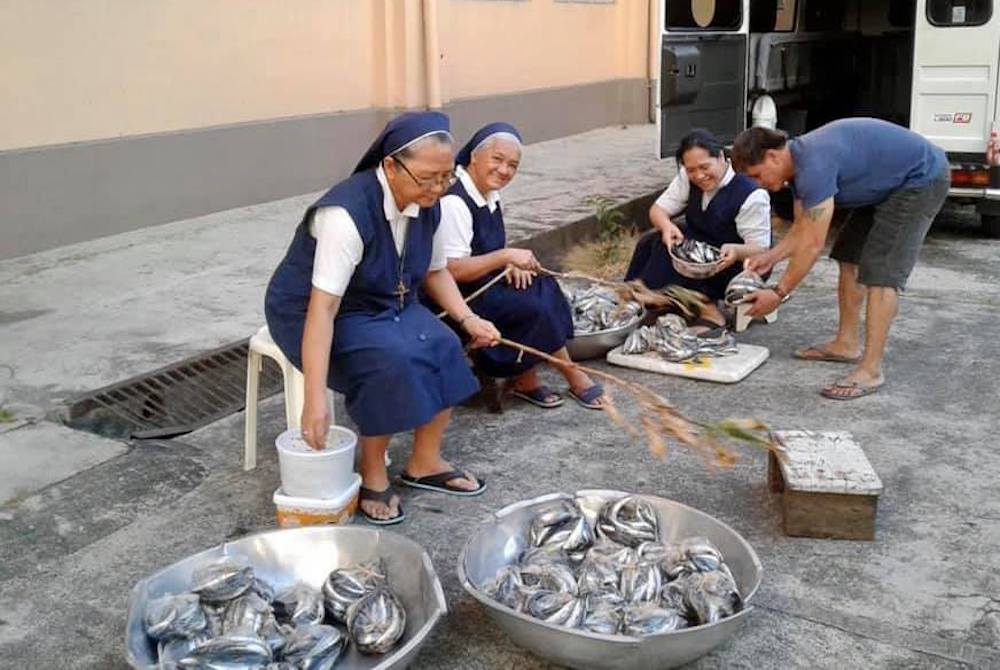 The Missionary Sisters Servants of the Holy Spirit-Northern Province provide seafood to day laborers, people whose jobs disappeared during the pandemic, in Quezon City, Philippines. (Sr. Angel C. Libron) Catholic sisters sitting in chairs in the street with baskets of fish to give away