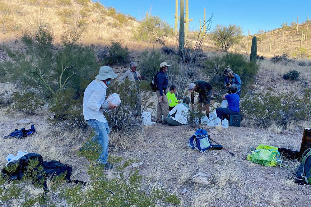 Felician Sr. Maria Louise Edwards (in neon yellow shirt, seated in background) writes messages to migrants on water bottles with volunteers in the Sonoran Desert near Ajo, Arizona. The messages include the dates of the water drop and encouraging words.