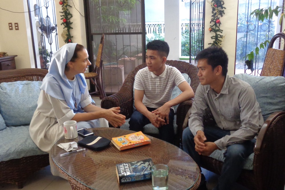 Catholic sister in a habit sits and talks to two young Filipino men