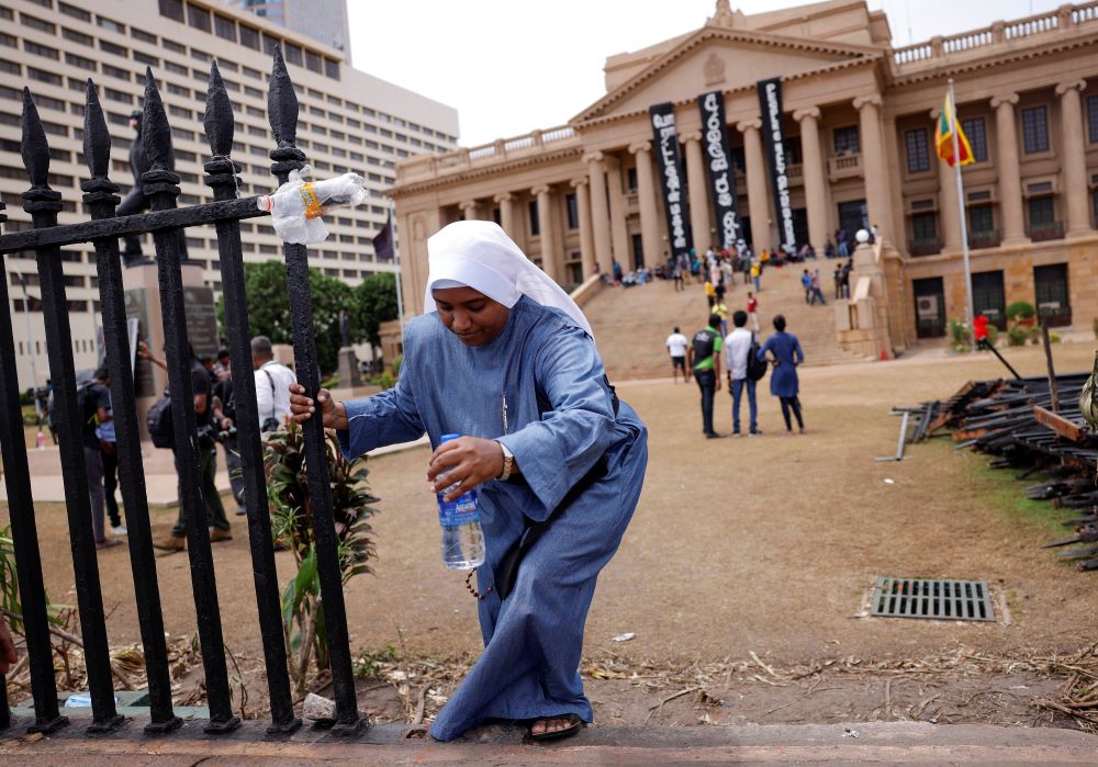A nun climbs over the boundary wall at the Presidential Secretariat in Colombo, Sri Lanka, July 15, after an official announced the resignation of President Gotabaya Rajapaksa, amid the country's economic crisis. (CNS/Reuters/Dinuka Liyanawatte)