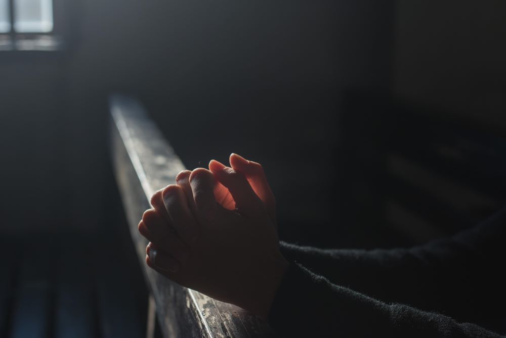Hands clasped in prayer rest on rail (Pixabay/Himsan)