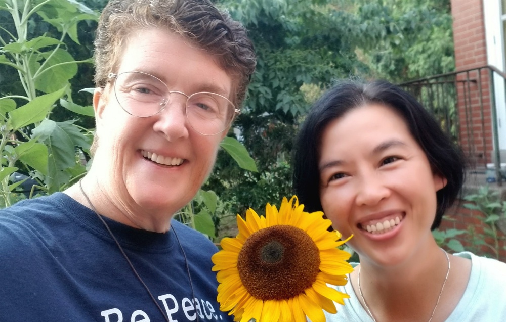 Dominican of Peace candidate Cathy Buchanan, left, and Lover of the Holy Cross Sr. AnHoa Nguyen admire a sunflower in the convent garden on Aug. 8. (Provided photo)