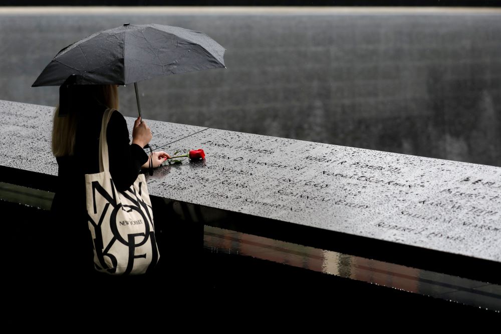 A person in New York City stands in the rain with a red rose at the 9/11 Memorial ahead of the 20th anniversary of the September 11 attacks in Manhattan. (CNS/Reuters/Andrew Kelly)