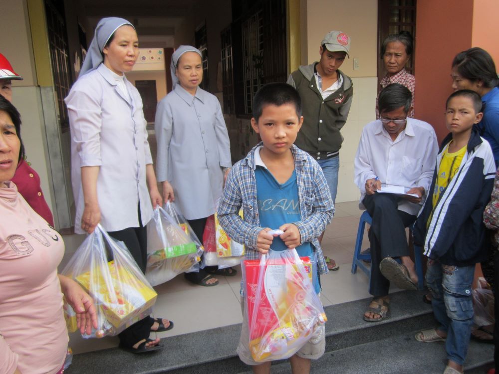Le Dinh Thuan (center), an orphan who lives with his grandmother in Hue, receives cake and cooking oil from St. Paul de Chartres nuns Sept. 7. (GSR photo/Joachim Pham)
