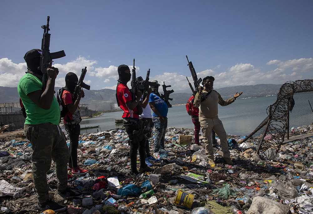 Flanked by members of the G9 gang coalition, leader Jimmy Cherizier, aka Barbecue, right, talks to reporters near the perimeter wall that encloses Terminal Varreux, the port owned by the Mevs family, in Port-au-Prince, Haiti, in October 2021. (AP)