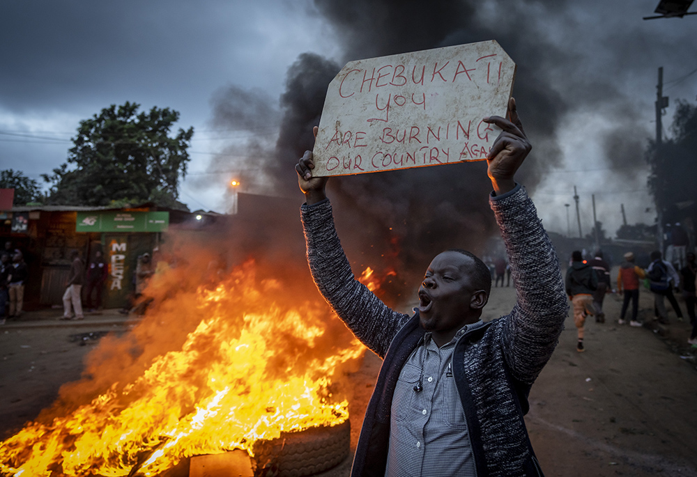 A supporter of presidential candidate Raila Odinga holds a placard referring to electoral commission chairman Wafula Chebukati, while shouting "No Raila, no peace", next to a roadblock of burning tires Aug. 15 in Nairobi, Kenya. (AP photo/Ben Curtis)