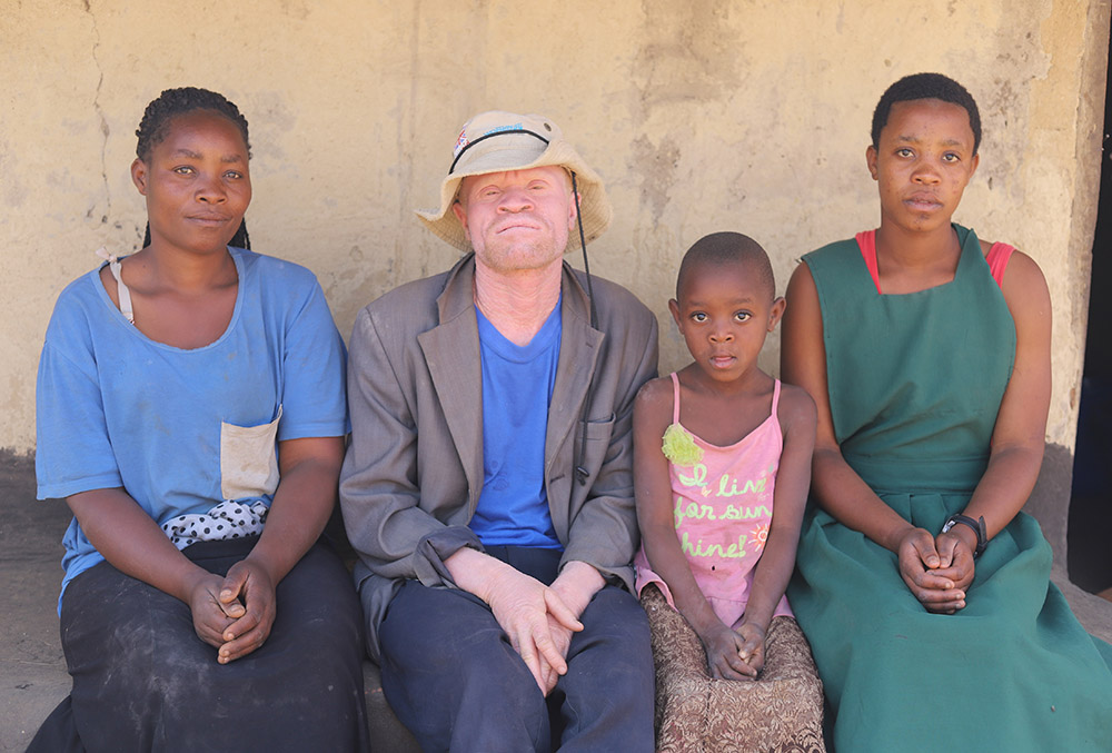 Musa Wiladi, 38, with his wife and his two daughters, sits outside their house in Mtendere, Malawi. (GSR photo/Doreen Ajiambo)