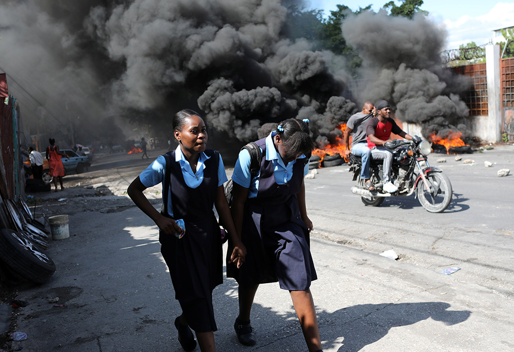 Schoolgirls walk past a burning street barricade during demonstrations Nov. 25, 2021, against widespread kidnappings in Port-au-Prince, Haiti. (CNS/Reuters/Ralph Tedy Erol)