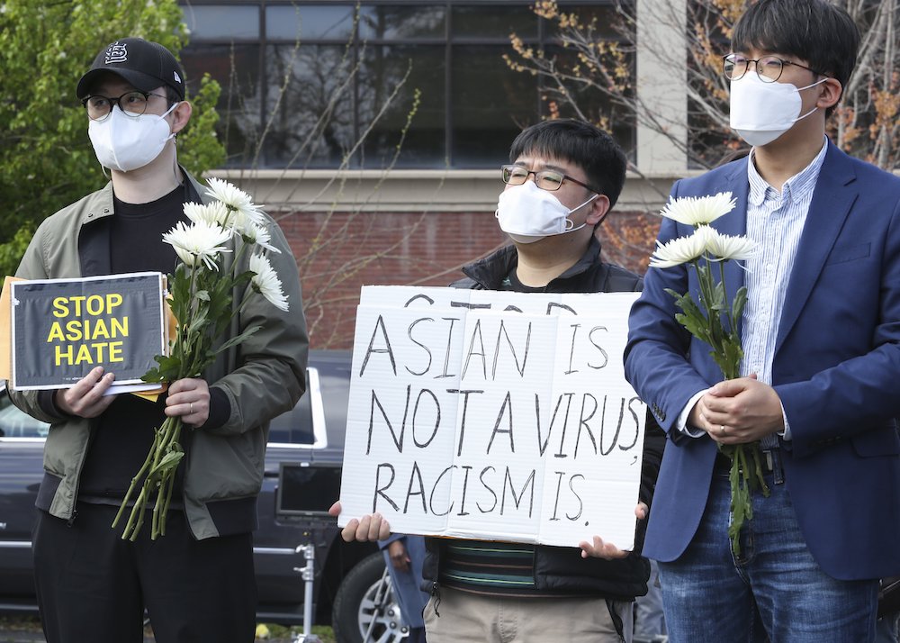 Three young Asian American men wearing masks; one is holding a sign, "Stop Asian Hate," and another's sign says "Asian is not a virus. Racism is."