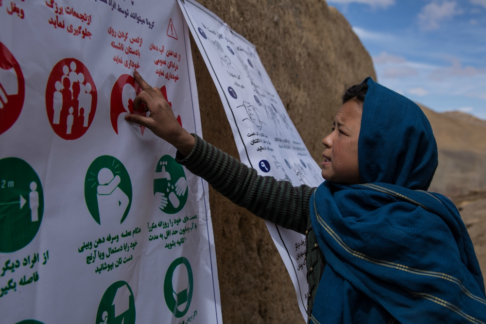 Mina, 11, reads a Catholic Relief Services sign warning about the symptoms and preventions of the coronavirus in Largurang village, Bamyan, Afghanistan. (Courtesy of Catholic Relief Services / Stefanie Glinski)