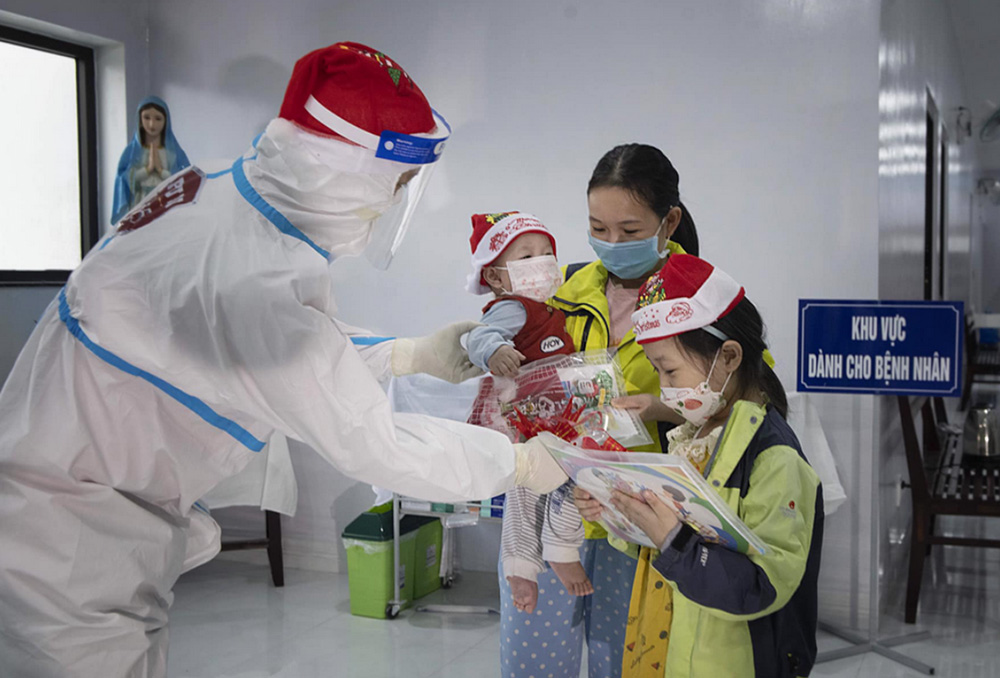 A sister in medical gear offers Christmas gifts to a woman and her two children at Kim Long Charity Clinic in Kim Long ward in Hue, Vietnam, at Christmas. (Courtesy of the Filles de Marie Immaculée)
