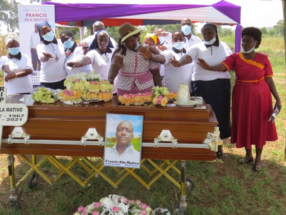 Women, including sisters in habits hold their hands over the casket to pray under a tent