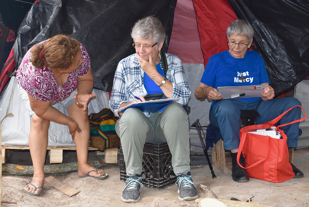 Notre Dame de Namur Srs. Mary Alice McCabe, center, and Jeanette Braun, right, use a tent as a makeshift office from which they helped the families at a migrant camp in Matamoros, Mexico, fill out their asylum applications in 2019. (Courtesy of Mary Alice Notre Dame de Namur Srs. Mary Alice McCabe, center, and Jeanette Braun, right, use a tent as a makeshift office from which they helped the families at a migrant camp in Matamoros, Mexico, fill out their asylum applications in 2019. (Courtesy of Mary Alice