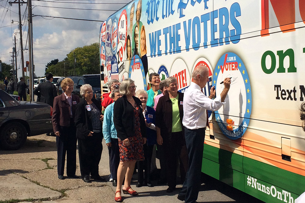 Joe Biden signs his name to the Network Nuns on the Bus official vehicle for the 2014 tour after speaking at the kickoff rally in front of the Iowa State Capitol in September 2014, when Biden was vice president. The nuns on the bus are behind him along wi