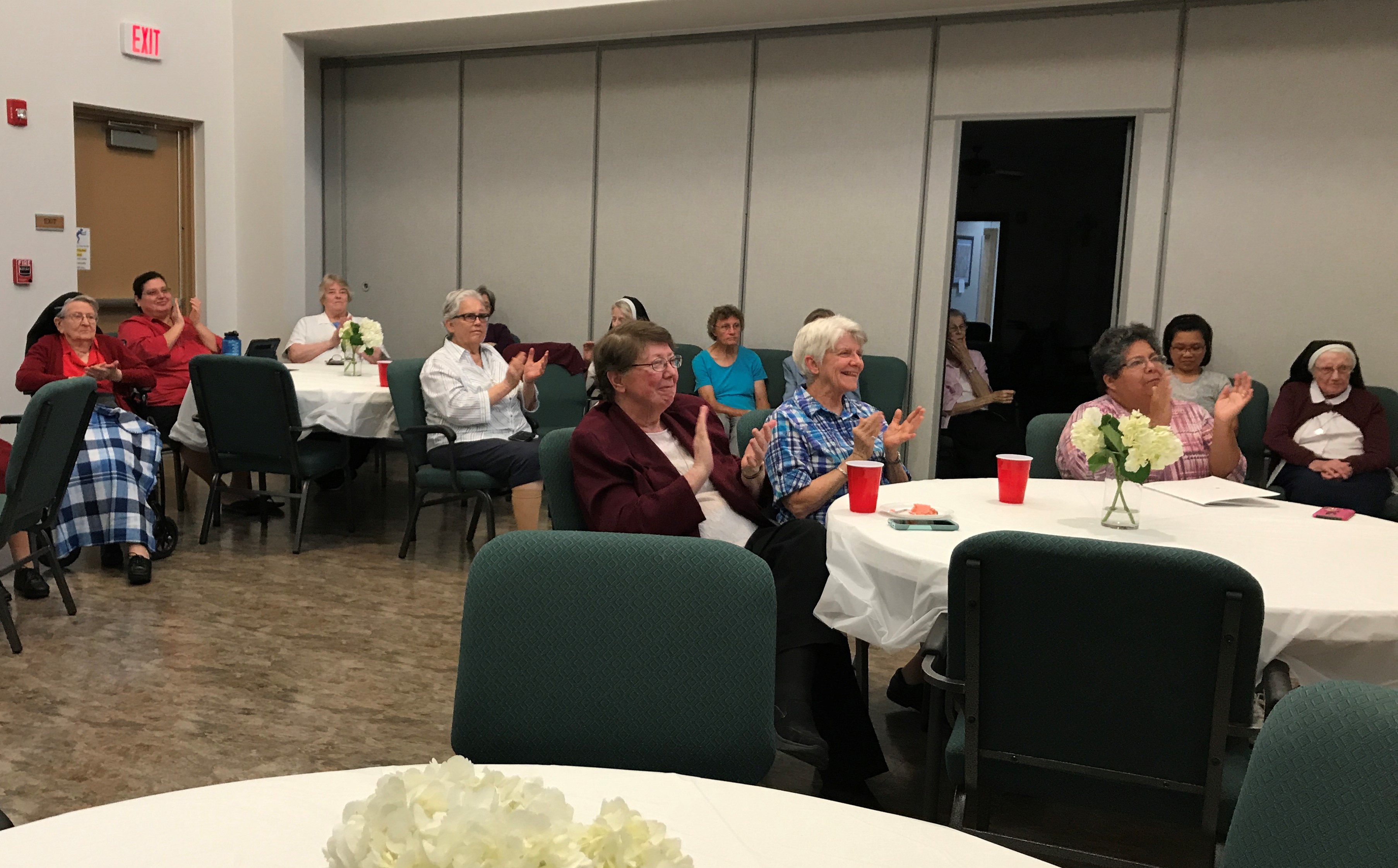 Sisters of the Incarnate Word and Blessed Sacrament, including Sr. Lou Ella Hickman, in the maroon jacket, applaud the performance of "Chavah's Daughters Speak," which the sisters viewed via livestream May 11 from the convent meeting room in Corpus Christ