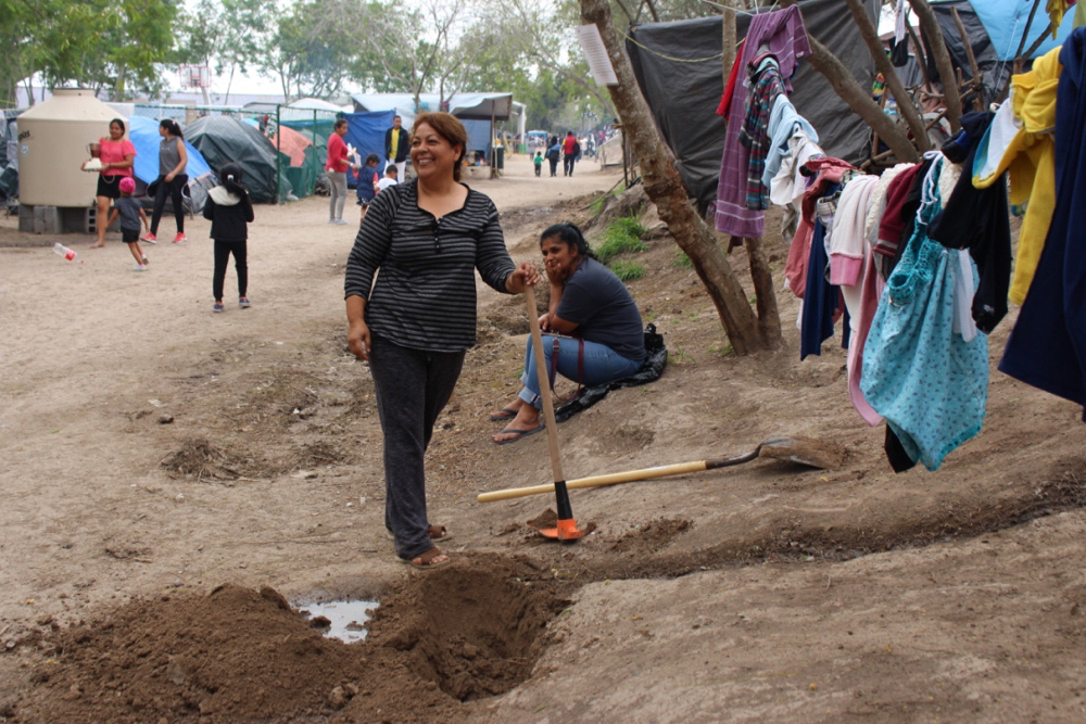 In the Matamoros camp on the Mexican side of the U.S. border, Esmeralda, a community leader from Honduras, pauses in wielding a pickaxe, digging a ditch to keep water runoff from her improvised kitchen from muddying the path below. (GSR/Tracy L. Barnett)