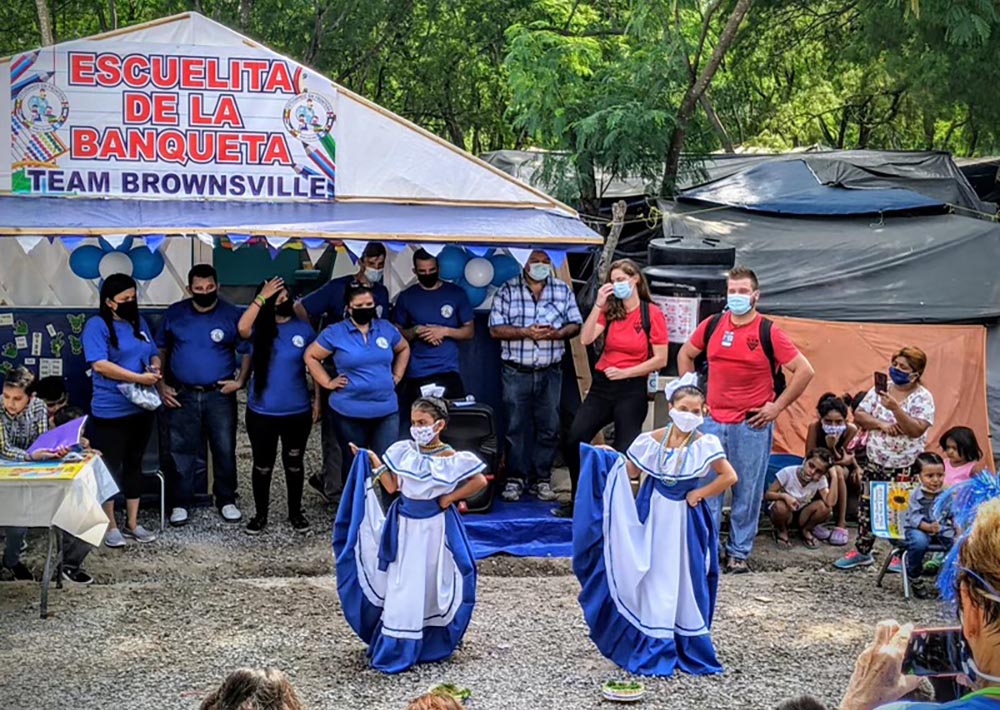 Children in blue and white dance at the school opening in the migrant camp in Matamoros, Mexico. (Courtesy of Jacinta Powers)