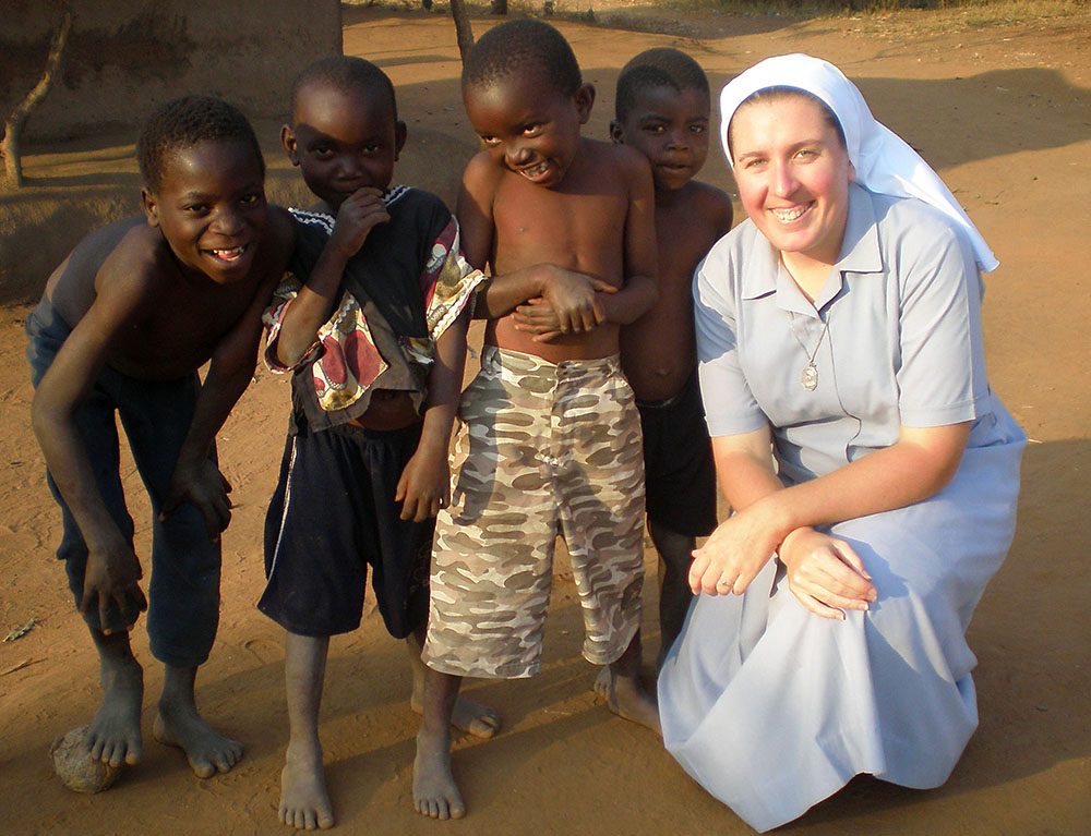 Sister Dwyer squatting next to four small children. They are all smiles. 