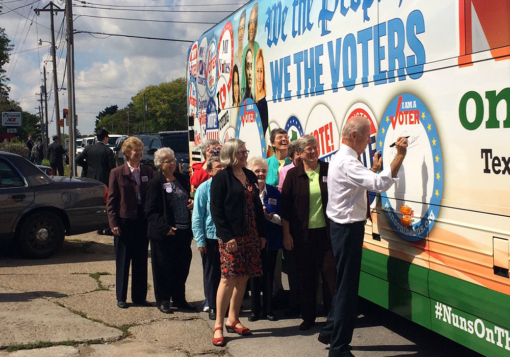 Vice President Joe Biden signs his name to the Network Nuns on the Bus official vehicle after speaking at the kickoff rally in front of the Iowa State Capitol in September 2014. Some of the Nuns on the Bus, including Sr. Simone Campbell, in red shoes, sta