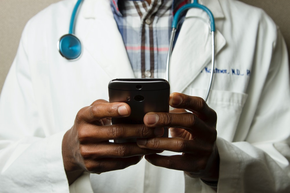 Image of a Black doctor with a smartphone (Unsplash/National Cancer Institutue)