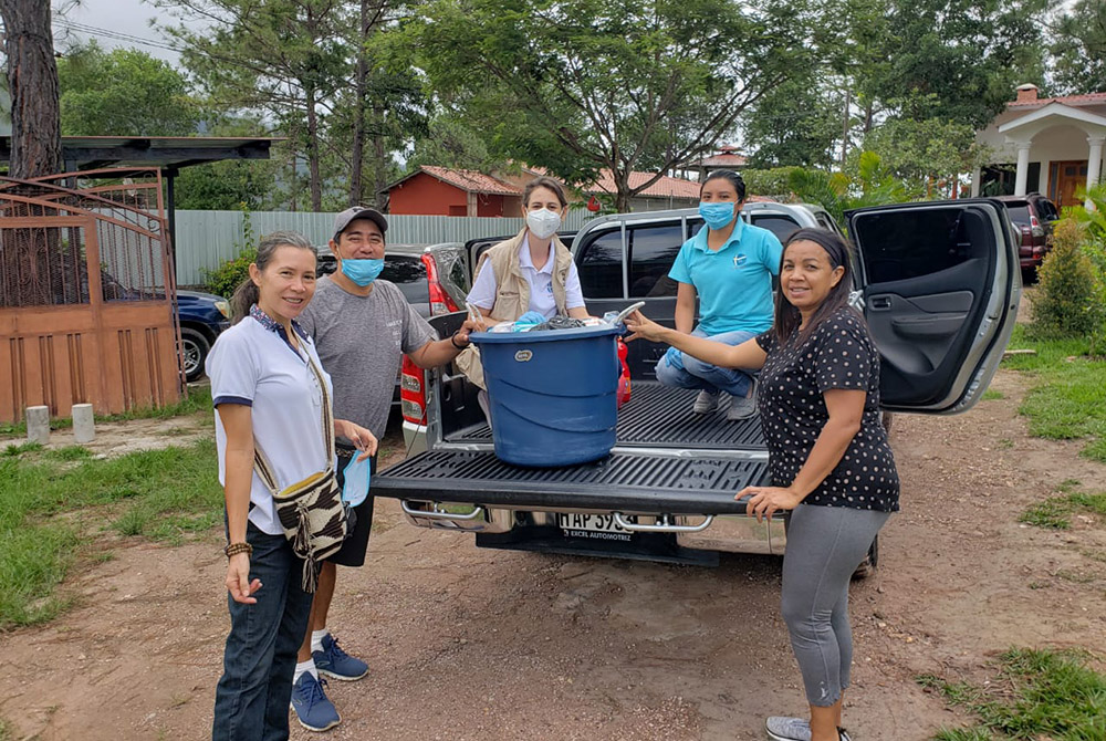 Members of the migrant center team sit on the bed of a truck, where a blue liquid tank rests; others are standing nearby. 