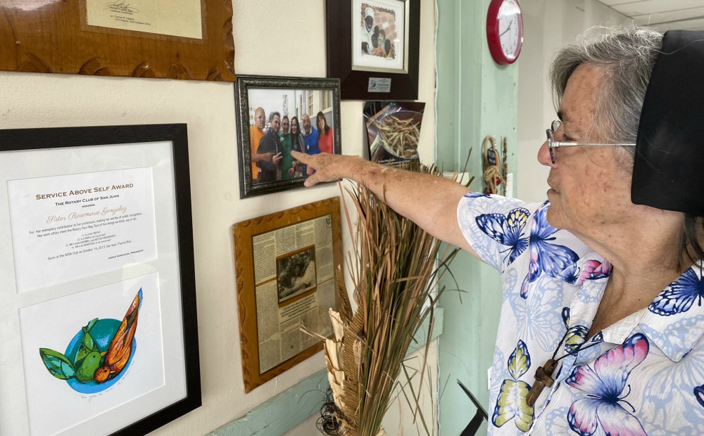 El Hogar del Buen Pastor de San Juan de Puerto Rico tiene una galería con artículos enmarcados sobre este centro y fotos grupales de los residentes. Aquí, la Hna. Rosemarie González recuerda a un grupo de personas, algunas de ellas ya fallecidas, que montaron un negocio juntas. (Foto: GSR/Soli Salgado)