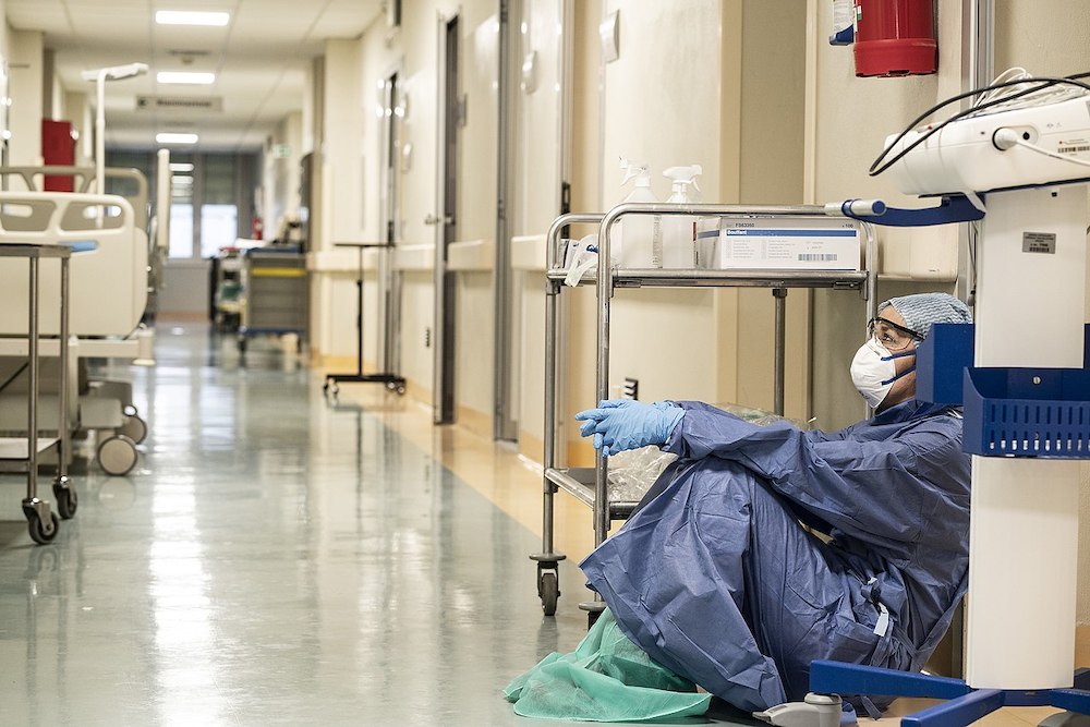 A health care worker in PPE sits exhausted in the hallway of the San Salvatore Hospital in Pesaro, Italy, at the end of a 12-hour shift of taking care of COVID-19 patients March 19, 2020