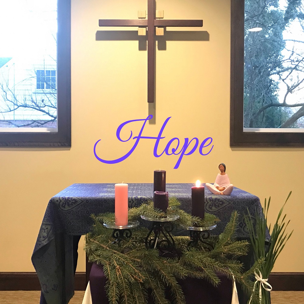Our motherhouse chapel's Advent wreath (Nicole Trahan) Image: An Advent wreath with one purple candle lit in front of an altar with a cross hanging above it. Superimposed over the image in purple is the word "hope."