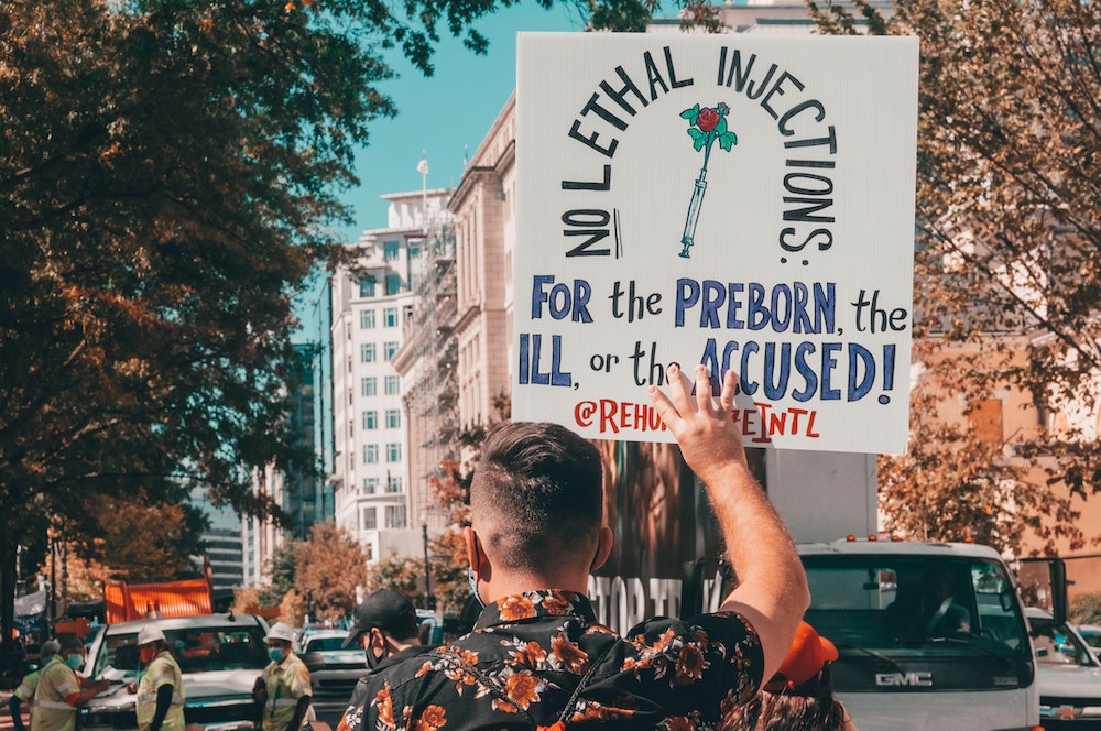 View of back of person holding sign that reads "No lethal injections for the preborn, the ill or the accused" (Unsplash Maria Oswalt) View of back of person holding sign that reads "No lethal injections for the preborn, the ill or the accused" (Unsplash Maria Oswalt)