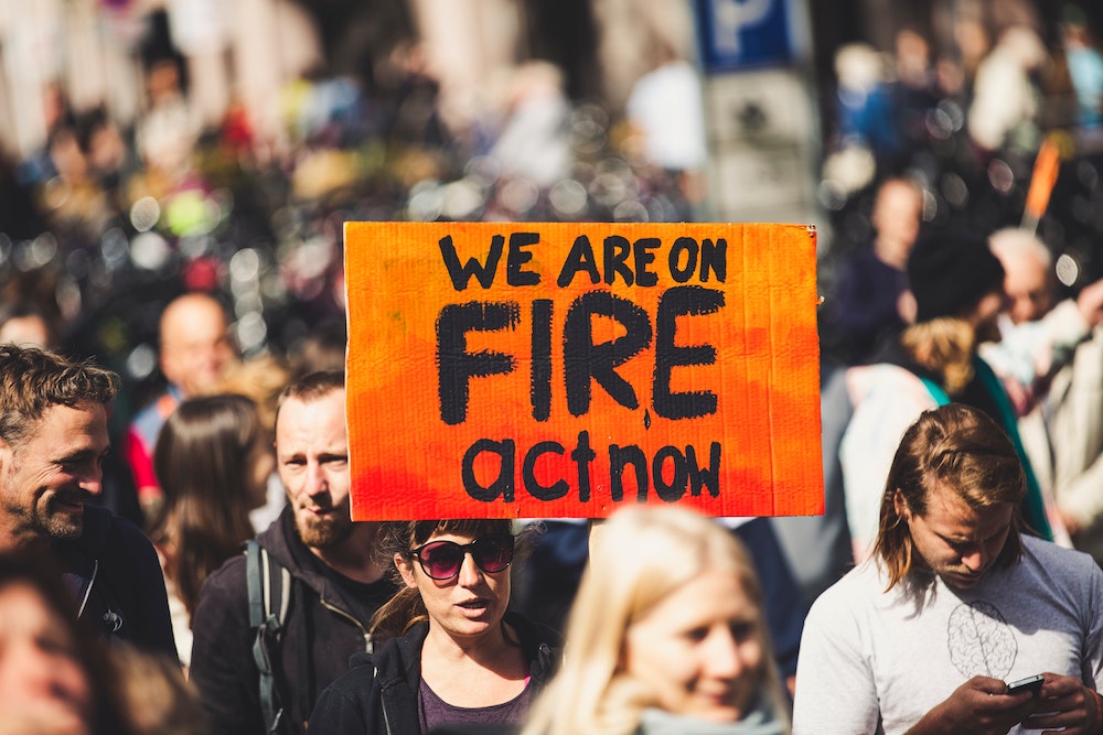 Demonstrators marching together, while a person holds a sign that reads "We are on fire, act now." (Unsplash/Markus Spiske) Demonstrators marching together, while a person holds a sign that reads "We are on fire, act now." (Unsplash/Markus Spiske)