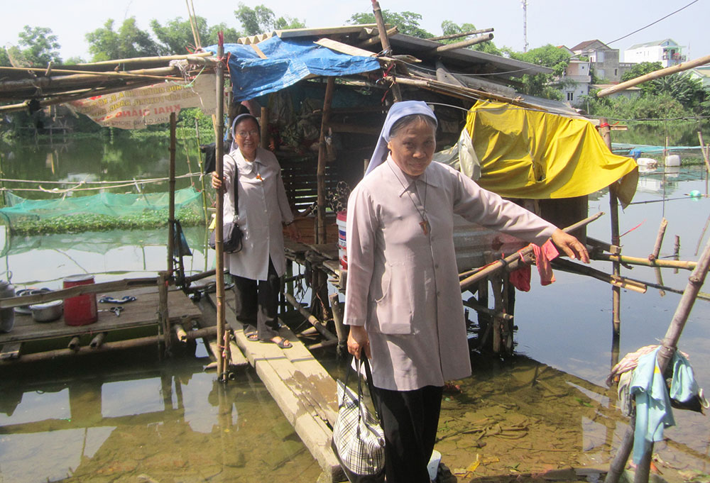 Sr. Maria Truong Thi Minh Yen, right, and another sister from the Daughters of Mary Immaculate visit a family living in a shelter on the Huong River Jan. 31. (Joachim Pham)