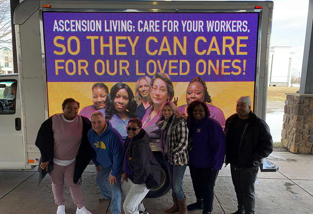 Ascension Living workers at Our Lady of Peace pose in front of a billboard. (Courtesy of 1199SEIU United Healthcare Workers East)