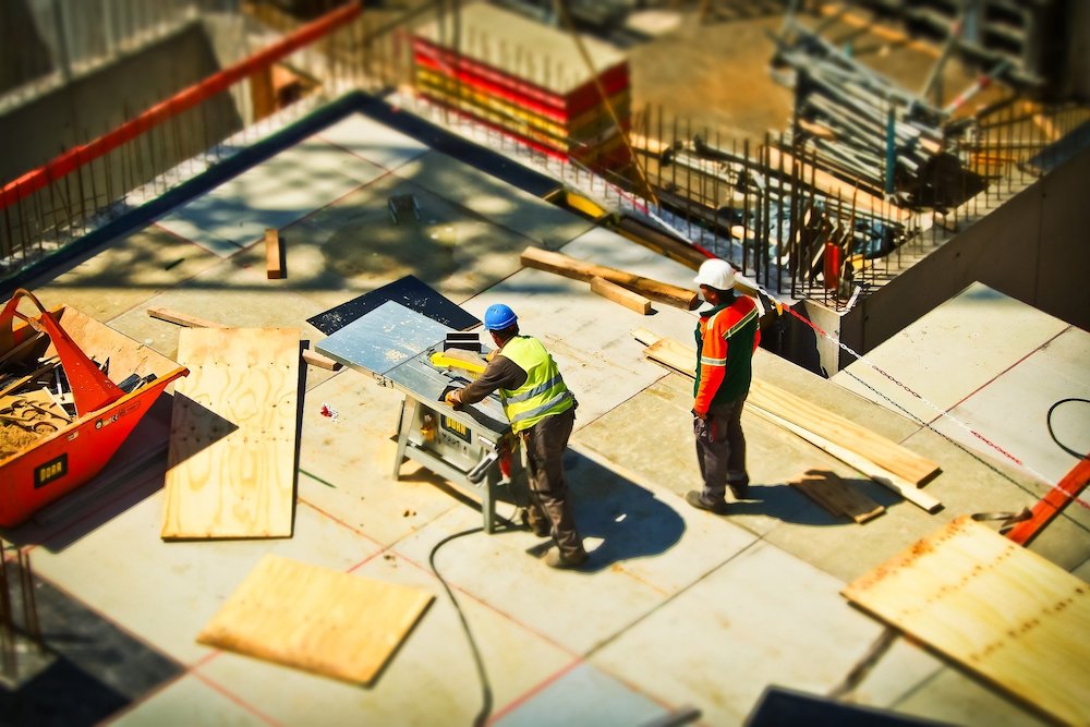 Overhead view of two men in bright safety gear sawing plywood for flooring at a construction site
